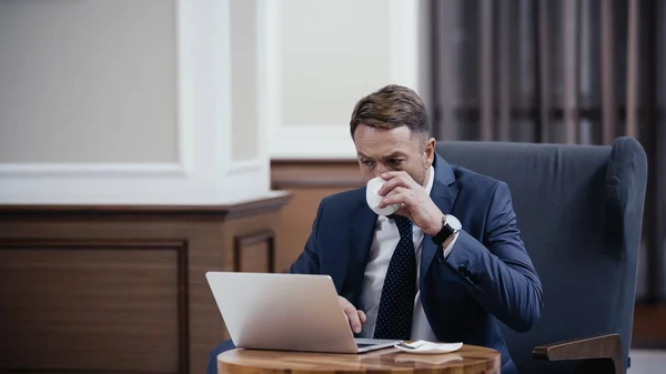 Geschäftsmann im Anzug trinkt Kaffee und benutzt Laptop in der Lobby eines Restaurants — Stockfoto