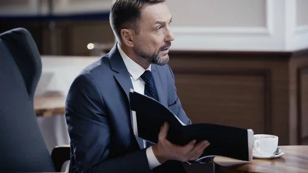 Geschäftsmann hält Papiermappe in der Hand und schaut im Restaurant weg — Stockfoto