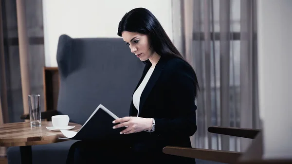 Brunette businesswoman looking at paper folder with documents in restaurant — Stock Photo