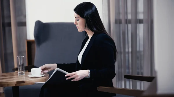 Businesswoman with paper folder reaching cup of coffee in restaurant — Fotografia de Stock