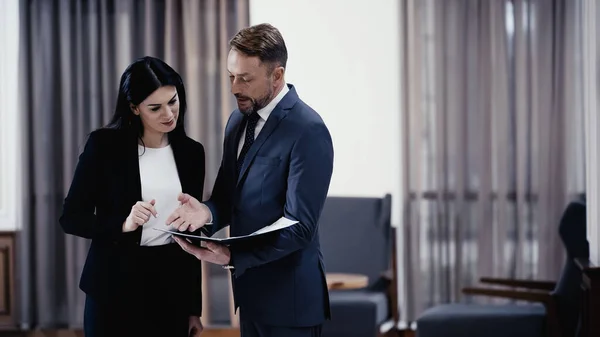 Businessman pointing with hand at documents near woman in lobby of restaurant - foto de stock