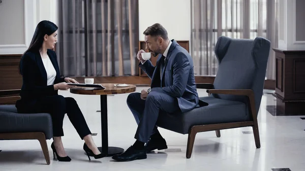 Businessman drinking coffee during business meeting with woman in restaurant lobby — Stock Photo