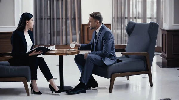 Geschäftsfrau hält Papiermappe neben Geschäftsmann mit Tasse Kaffee in Restaurant-Lobby — Stockfoto
