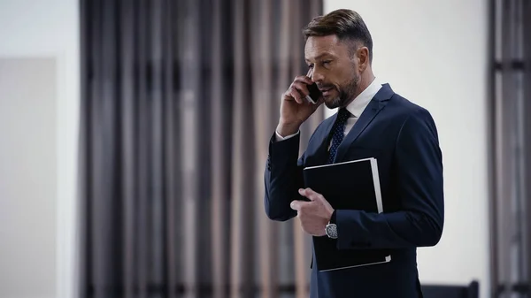 Businessman with paper folder talking on smartphone in lobby of restaurant — Fotografia de Stock