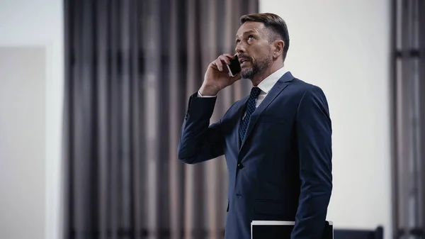 Businessman with paper folder talking on cellphone in lobby of restaurant — Stock Photo