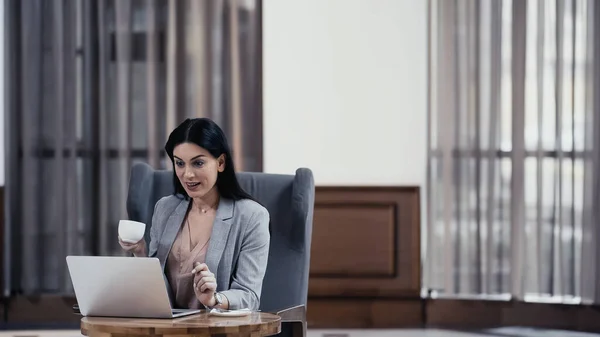 Erstaunte Freiberuflerin hält Tasse Kaffee neben Laptop auf Tisch im Restaurant — Stockfoto