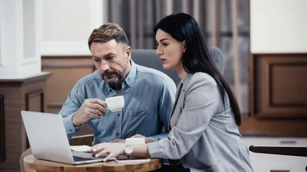 Business partners working on laptop near cups of coffee in lobby of restaurant — Fotografia de Stock