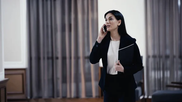 Businesswoman with paper folder talking on smartphone in lobby of restaurant - foto de stock