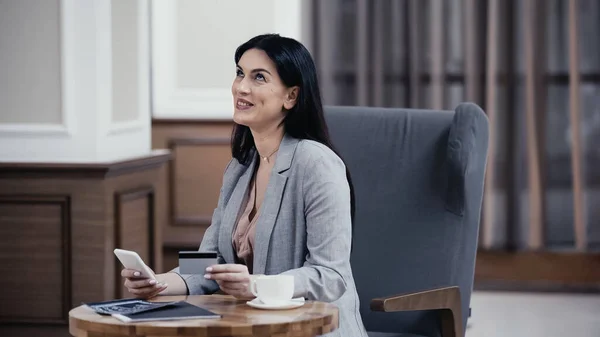 Happy businesswoman paying with credit card and smartphone in restaurant lobby — Foto stock