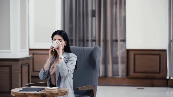 Бізнес-леді розмовляє по смартфону і п'є каву у фойє ресторану — стокове фото