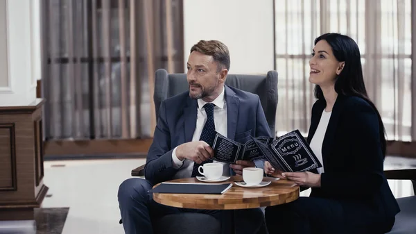 Happy business partners holding menu near coffee on table in restaurant lobby — Photo de stock