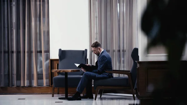 Geschäftsmann im Anzug sitzt auf Sessel und schaut sich Dokumente an — Stockfoto