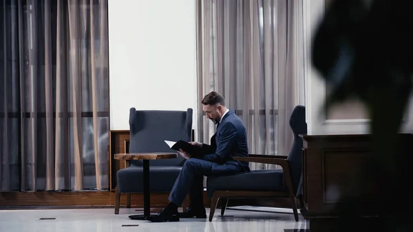 Businessman in suit sitting on armchair and looking at documents — Stock Photo