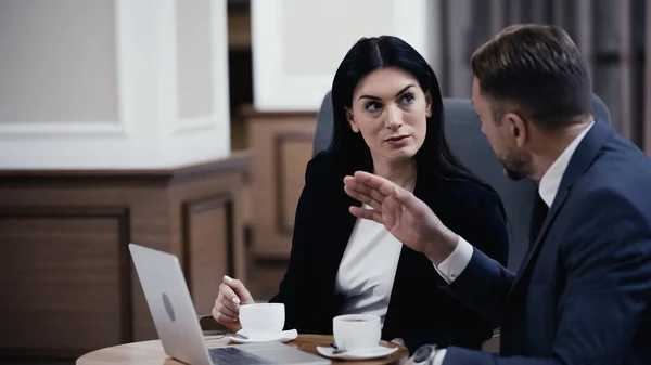 Businessman and businesswoman looking at each other and discussing work near laptop in restaurant — Foto stock