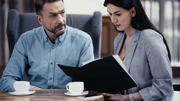 Businessman looking at woman with paper folder near cups of coffee on table — Foto stock