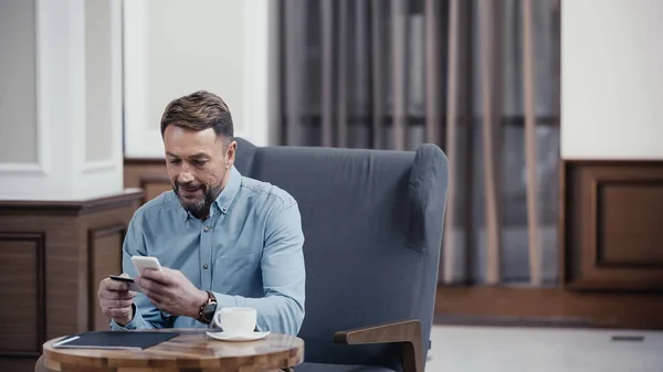 Mann bezahlt mit Kreditkarte und Handy in Lobby eines Restaurants — Stockfoto