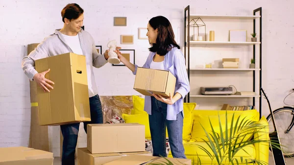 Hombre sonriente dando estatuilla a la mujer feliz mientras está de pie con cajas en un nuevo hogar - foto de stock