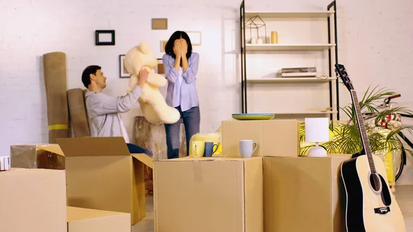 Mann hält Teddybär nahe Freundin und verdeckt Augen im Wohnzimmer — Stockfoto