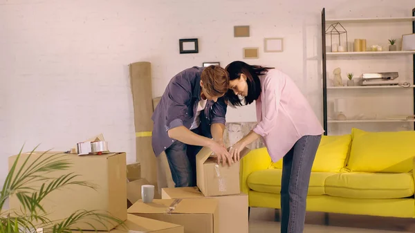 Веселая пара распаковывает коробку в новом доме — стоковое фото