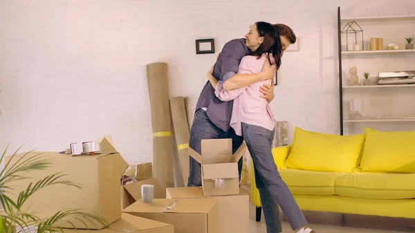 Happy couple hugging near carton boxes in new home — Stock Photo