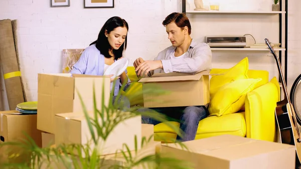 Hombre y mujer placas de embalaje en cajas de cartón en el sofá - foto de stock