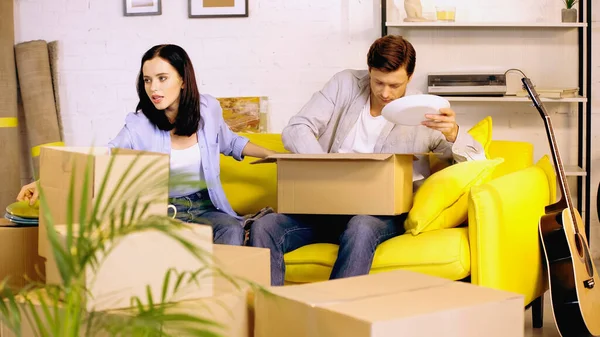 Couple packing plates in carton boxes on couch — Stock Photo