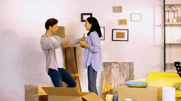 Mujer asombrada mirando novio con las manos extendidas en nuevo hogar - foto de stock