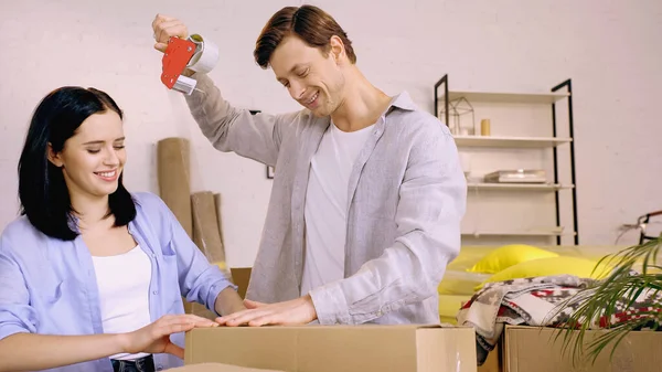 Happy couple using scotch tape while packing box — Stock Photo