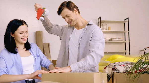 Happy couple using scotch tape while packing box — Stock Photo