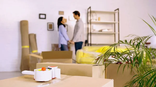 Scotch tape on boxes near blurred couple holding hands in new home — Stock Photo