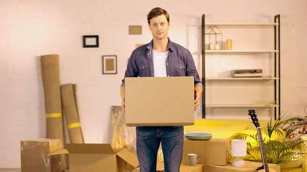 Young man holding cardboard box in new home — Stock Photo