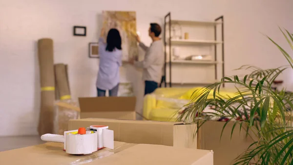 Cinta adhesiva en cajas cerca borrosa pareja colgando pintura en un nuevo hogar - foto de stock
