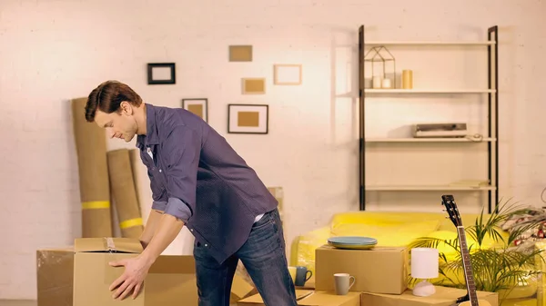 Young man putting cardboard box in new home — Stock Photo