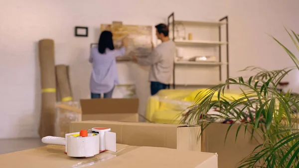 Scotch tape on carton box near blurred couple hanging painting — Stock Photo