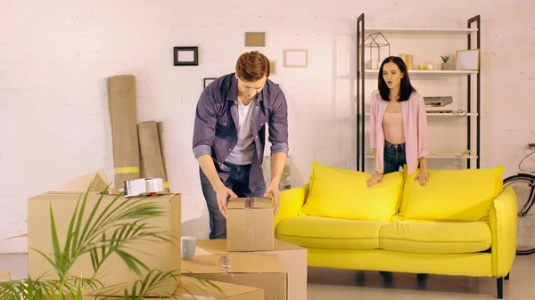 Женщина разговаривает, глядя на парня распаковывая коробку в новом доме — стоковое фото