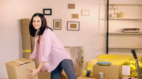 Счастливая женщина принимает картонную коробку в новом доме — стоковое фото