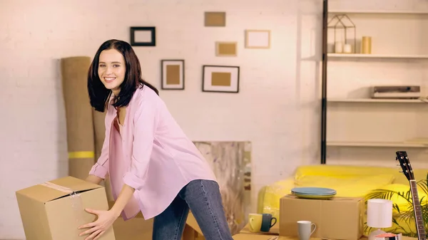 Mulher feliz levando caixa de papelão em nova casa — Fotografia de Stock