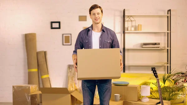 Jovem feliz segurando caixa de papelão em nova casa — Fotografia de Stock