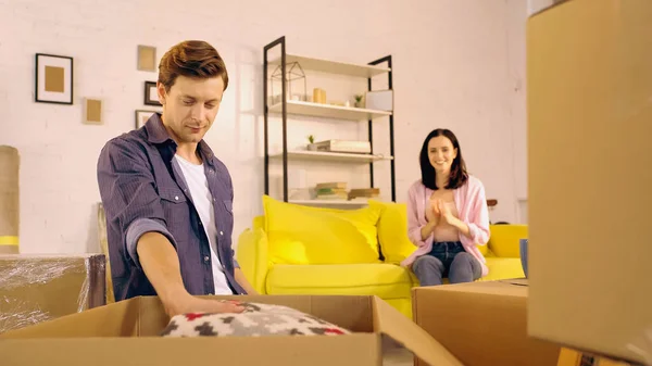 Man unpacking blanket near blurred and cheerful girlfriend on couch — Stock Photo