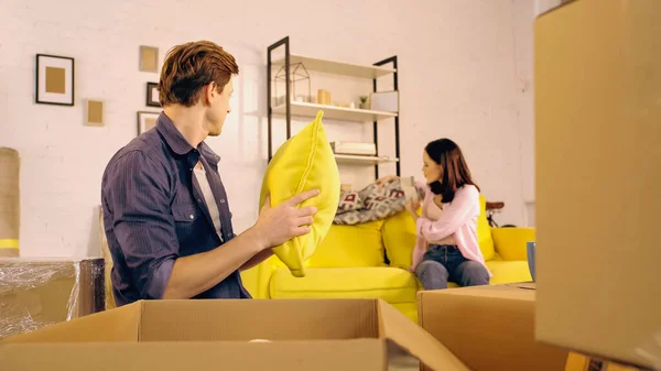 Man unpacking pillow near blurred and girlfriend sitting with blanket on couch — Stock Photo