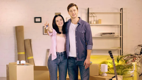 Усміхнена пара, що показує ключі біля коробки в новому будинку — стокове фото