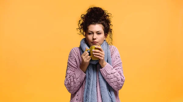 Mujer congelada sosteniendo taza de bebida caliente aislada en naranja - foto de stock