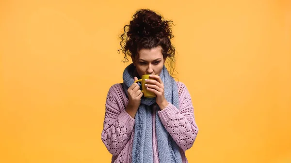 Femme congelée en pull tricoté buvant du thé isolé sur orange — Photo de stock
