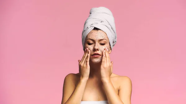 Woman with naked shoulders and towel on head applying face mask isolated on pink — Stock Photo