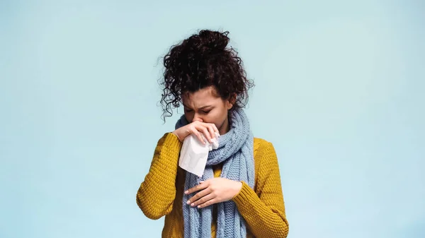 Femme malade en pull chaud essuyant nez avec serviette en papier isolé sur bleu — Photo de stock