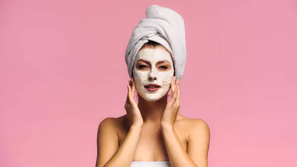 Femme avec serviette sur la tête regardant la caméra tout en appliquant un masque isolé sur rose — Photo de stock