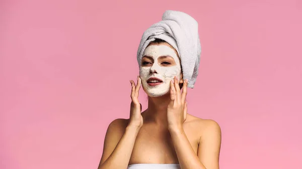 Mulher com ombros nus olhando para longe ao aplicar máscara facial isolada em rosa — Fotografia de Stock