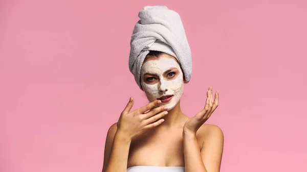 Young woman looking at camera while applying clay mask isolated on pink — Stock Photo
