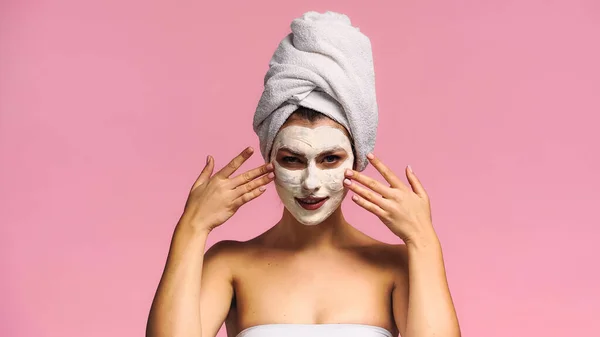 Jeune femme regardant la caméra tout en appliquant un masque en argile isolé sur rose — Photo de stock