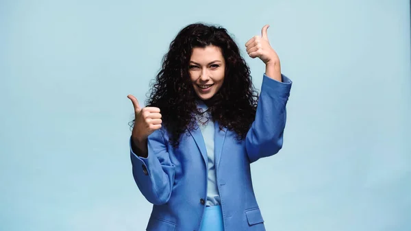 Excited woman looking at camera and showing thumbs up isolated on blue — Stock Photo